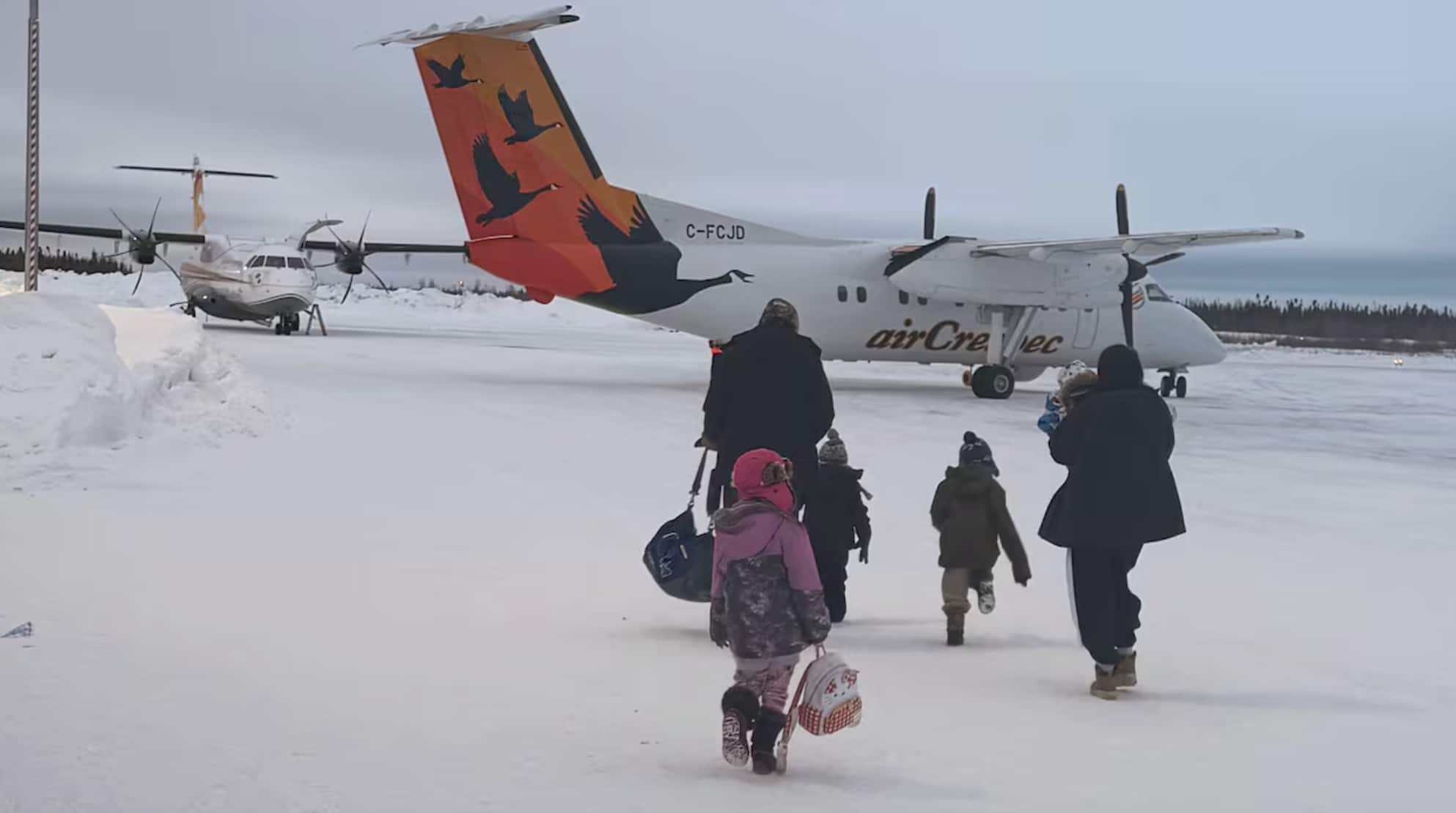 A family walks toward a small plane on a snowy tarmac.
